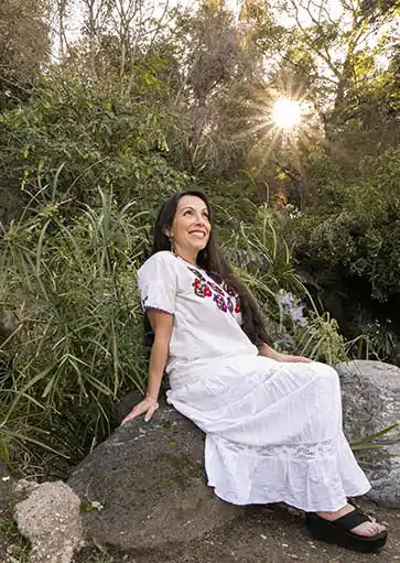 Erika Buenaflor in a white dress sitting on a rock