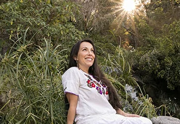 Erika Buenaflor in a white dress sitting on a rock